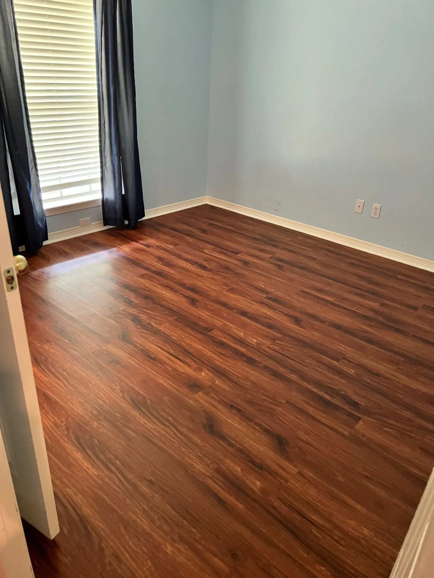 A bedroom finished in dark walnut LVP with white baseboards